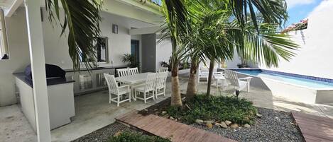 A patio with a dining table and chairs, a small pool, and palm trees.