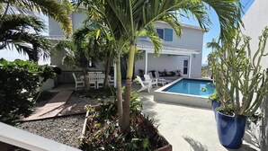 A pool area with a white building, palm trees, and potted plants.