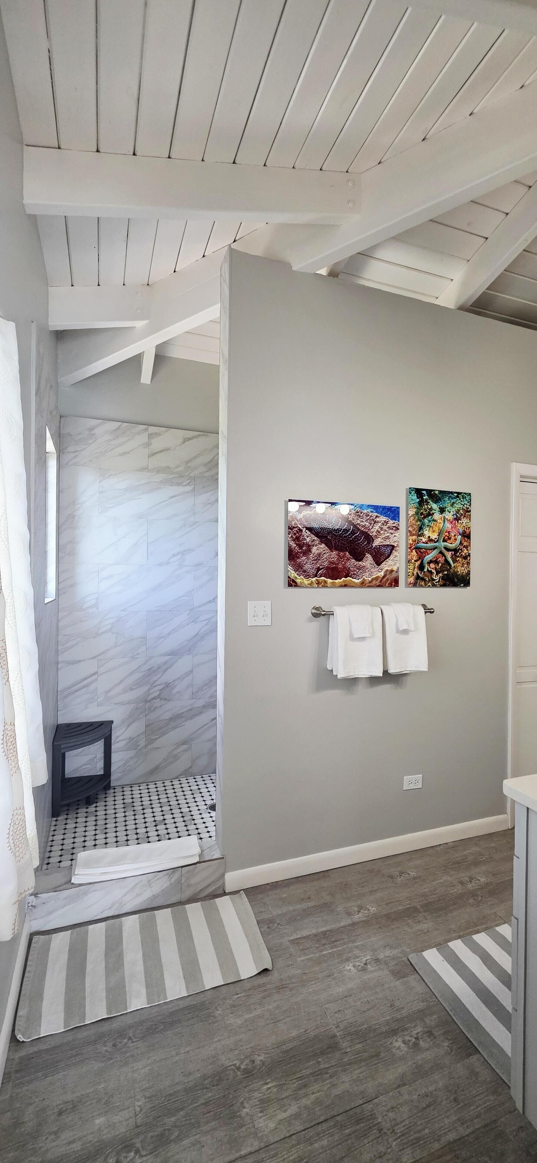 A bathroom with a shower area, marble tiles, a wooden ceiling, and two framed pictures on the wall.