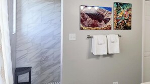 A bathroom with a shower area, marble tiles, a wooden ceiling, and two framed pictures on the wall.