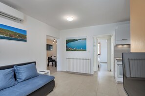 Uma sala de estar moderna com sofá, área de jantar, cozinha e corredor que leva a outro quarto.