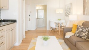A modern kitchen with white cabinets and a black countertop, a dining area with a white table and chairs, and a living room with a brown sofa and a white coffee table. - Stylish 1BR Suite w/ Kitchen & Balcony Near Universal & Epic Universe (Orlando)