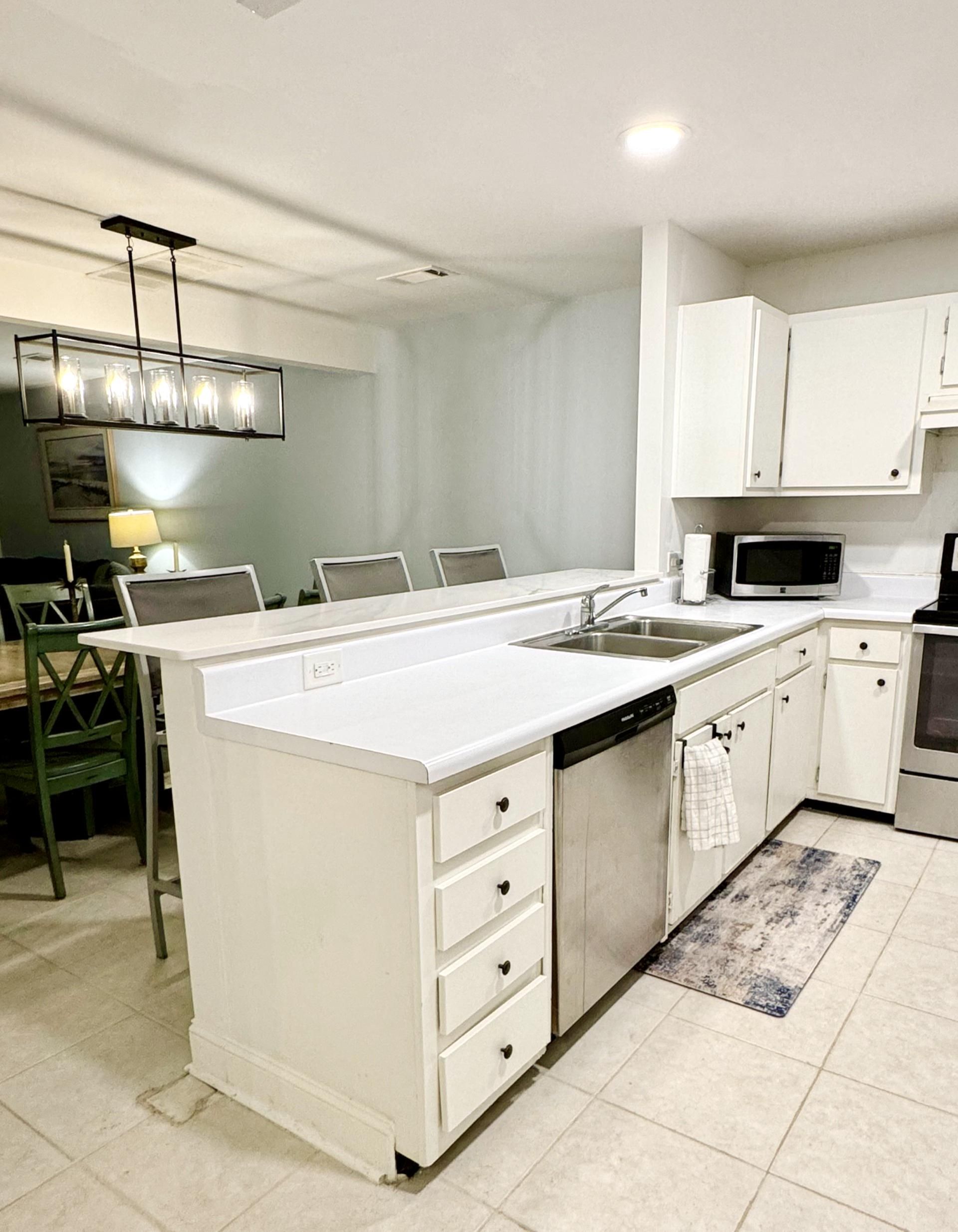A modern kitchen with a central island, white cabinetry, a built-in microwave, and a dining area with chairs and a table.