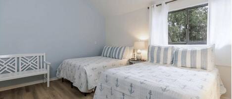 A bedroom with two beds, a white bench, and a window with curtains.