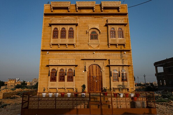 A large, ornate building with multiple arched windows and a central door, surrounded by a low wall and potted plants. - Hotel The Ginger House (Jaisalmer)