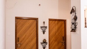 En hall med ett rutmönstrat golv, två dörrar av trä med mässingshandtag och väggmonterade lampor.