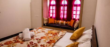 A bedroom with a bed, a window seat with cushions, and a decorative wall above the bed.