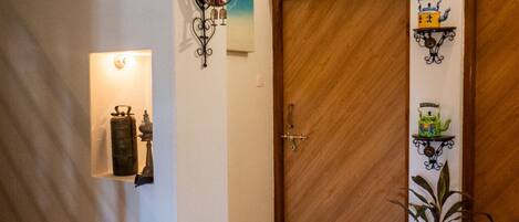 Un pasillo con piso a cuadros, puertas de madera y un estante en la pared con objetos decorativos.