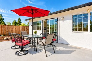 An outdoor patio with a glass table, four chairs, a red umbrella, and a wooden fence in the background. - Cozy Family Stay 3BR/2BA Home in Prime Milpitas Location (Milpitas)
