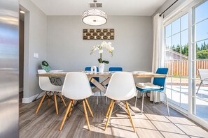 A dining area with a wooden table, white chairs, and a blue chair. There is a ceiling light fixture and a wall-mounted decorative piece above the table. - Cozy Family Stay 3BR/2BA Home in Prime Milpitas Location (Milpitas)