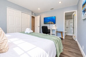 A hotel room with a bed, a desk, a chair, a shower area, and a painting on the wall. - Cozy Family Stay 3BR/2BA Home in Prime Milpitas Location (Milpitas)