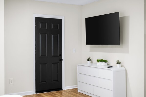 A room with a black door, a white dresser, and a mounted TV on the wall.