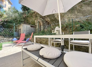 An outdoor seating area with a table and chairs, a large umbrella, and a stone wall backdrop. - Lovely Trilo with patio in Rapallo (Rapallo)