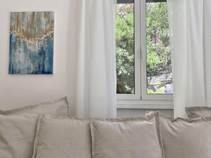 A room with a bed, a window with curtains, and a wall-mounted painting.