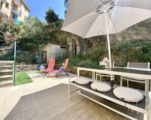 Un patio al aire libre con una mesa, sillas, un gran paraguas y un muro de piedra al fondo.