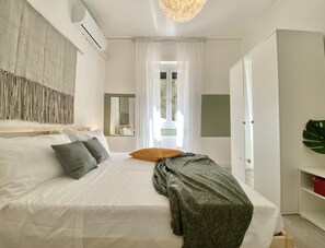 A bedroom with a bed, a bedside table, a mirror, and a window with curtains.