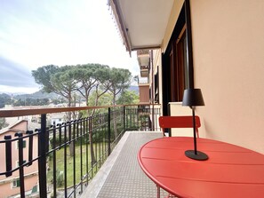 A balcony with a red table and a black lamp, overlooking a garden and buildings. - CasaViva - Central Wonderful Home in Santa M. (Santa Margherita Ligure)