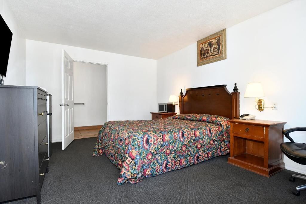Un dormitorio con cama, cómoda, mesita de noche con lámparas y una silla.