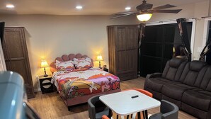 A bedroom with a bed, bedside lamps, a ceiling fan, a wardrobe, and a seating area with a table and chairs.