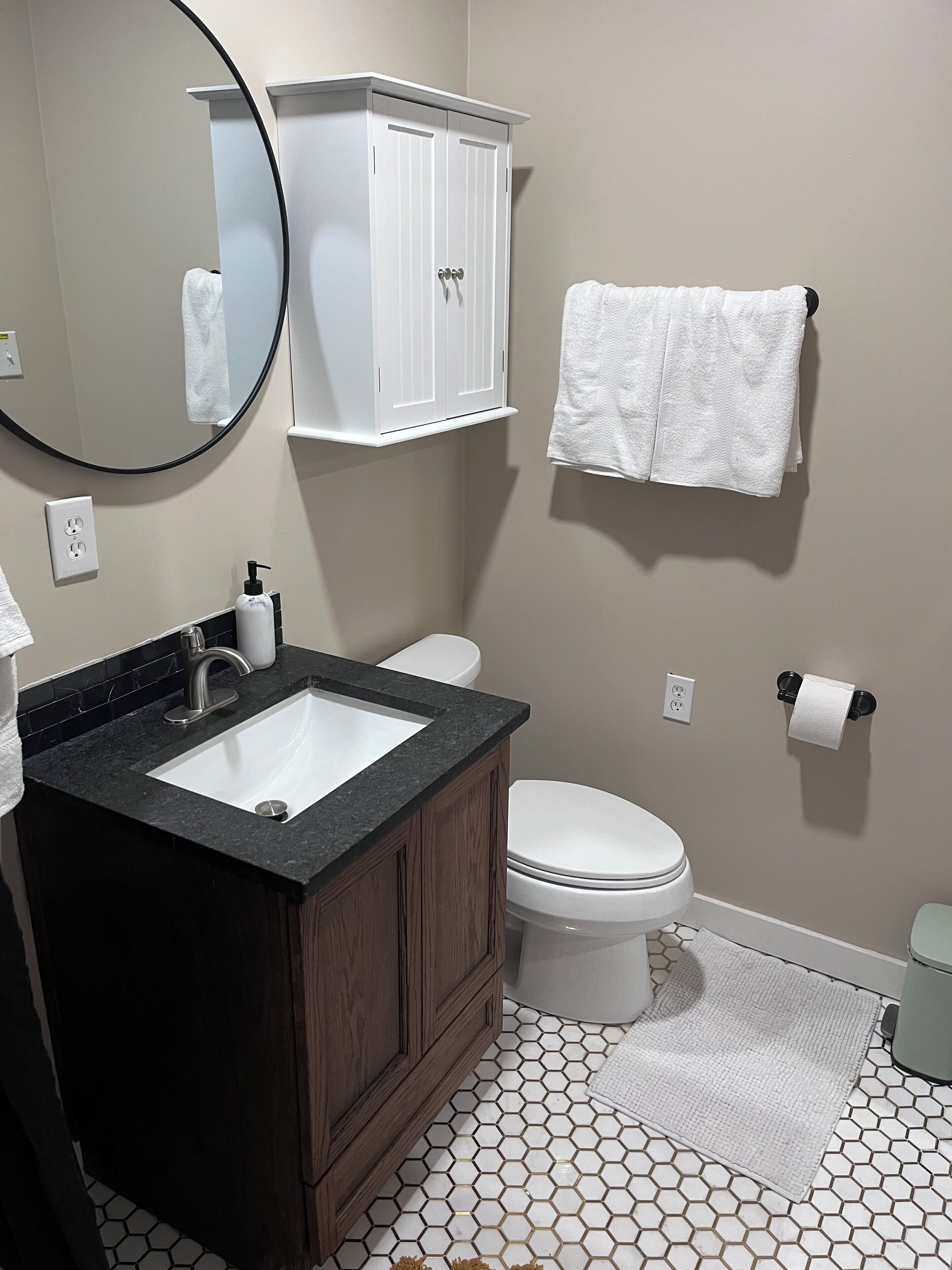 Un baño con lavamanos blanco, tocador de madera oscura, inodoro blanco y una toalla blanca colgada en la pared.