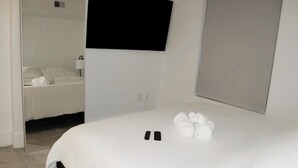 Ett hotellrum med en säng, en platt-TV som är monterad på väggen och en garderob med en spegel.
