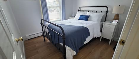 Een slaapkamer met een bed, nachtkastje, lamp en een raam met gordijnen.