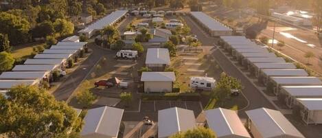 A large RV park with multiple RVs and trailers parked in rows, surrounded by trees and open spaces.