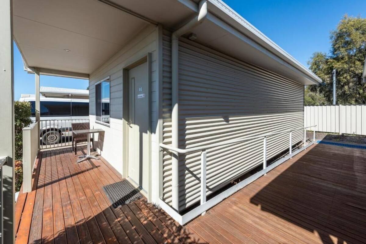 Un espace extérieur abrité doté d’une terrasse en bois, d’un coin salon couvert et d’un bâtiment avec une porte coulissante.