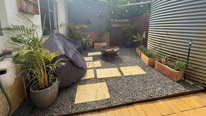 Eine Terrasse mit Feuerstelle, Kübelpflanzen und einer Wellmetallwand.