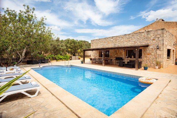 A swimming pool with lounge chairs, a stone building with outdoor seating, and a forested backdrop. - CA NA BEU - Fantastic rustic finca with private pool and free Wi‑Fi (Santanyí)