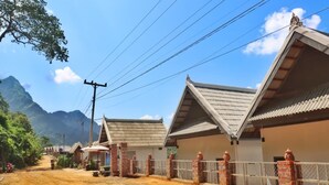 A rural road with traditional buildings, a dirt path, and a mountainous backdrop. - Dokchampa River View Villa (Nong Khiaw)