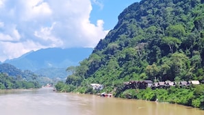 A river with houses on the banks, surrounded by lush greenery and mountains in the background. - Dokchampa River View Villa (Nong Khiaw)