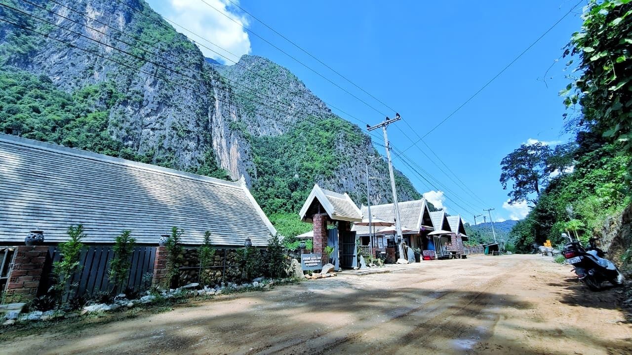 A rural road with buildings on one side and a mountain in the background.