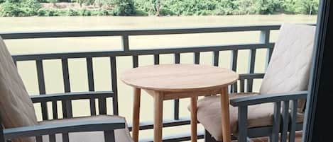 Un balcon avec deux chaises et une petite table, d’où l’on peut admirer une forêt verdoyante et une rivière.