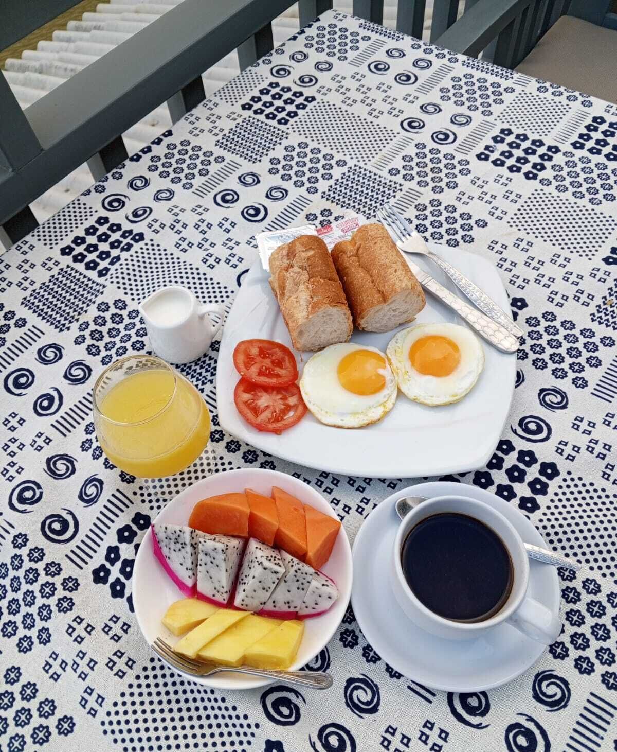 A table set with breakfast items including bread, eggs, tomatoes, a fruit plate, and a cup of coffee.