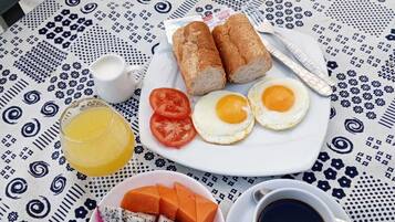 A table set with breakfast items including bread, eggs, tomatoes, a fruit plate, and a cup of coffee.