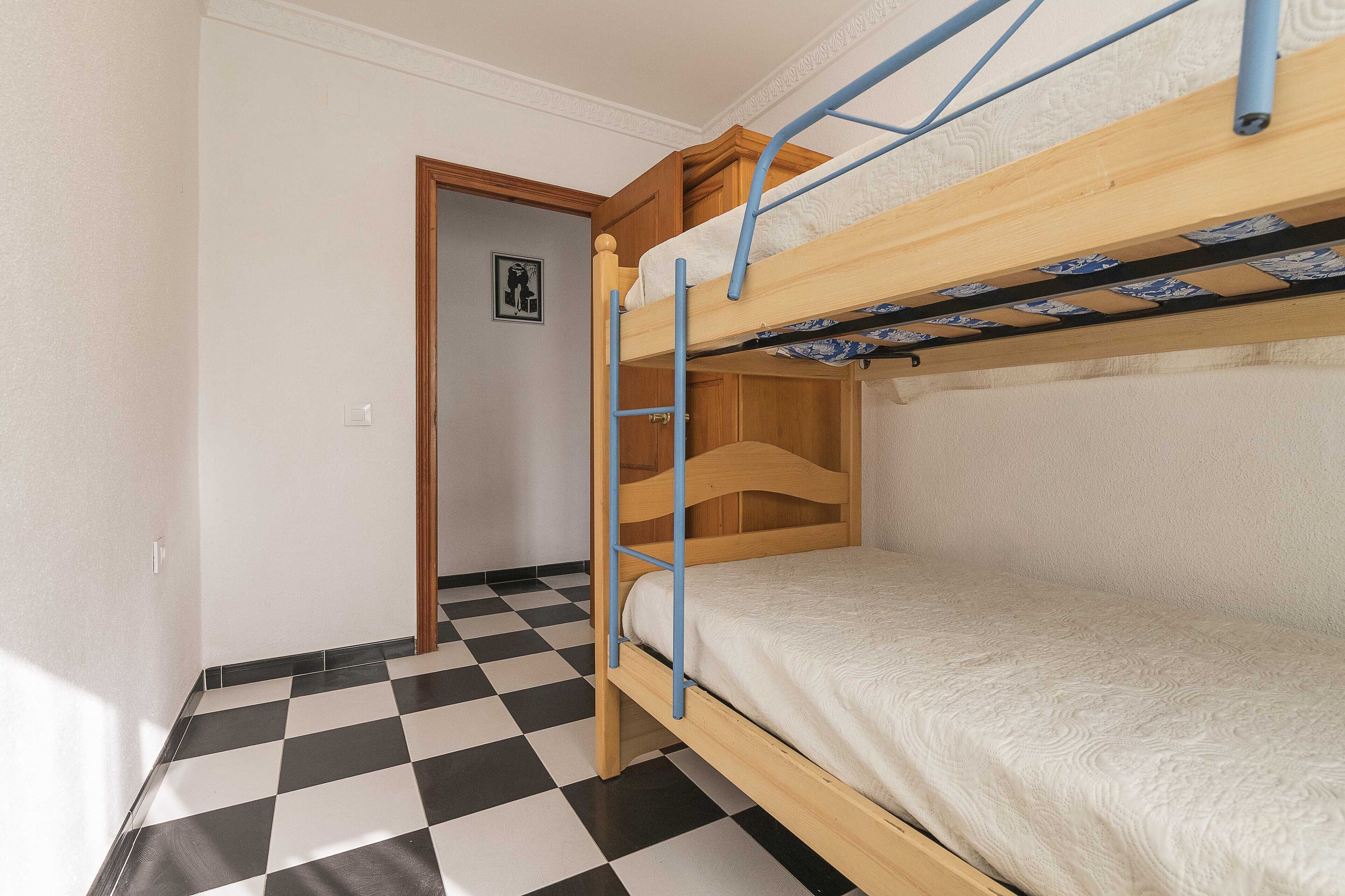 A bunk bed with a checkered floor and a door leading to another room.