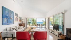 A modern living room with a large window overlooking the sea, a sofa, two red chairs, and a TV on a wooden cabinet. - ES TAMARELLS (S'ESTANYOL) - Villa by the Sea with Private Pool and Free Wi‑Fi (Artà)