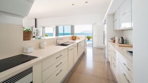 A modern kitchen with a view of the sea, featuring a large island, white cabinetry, and a sleek countertop. - ES TAMARELLS (S'ESTANYOL) - Villa by the Sea with Private Pool and Free Wi‑Fi (Artà)