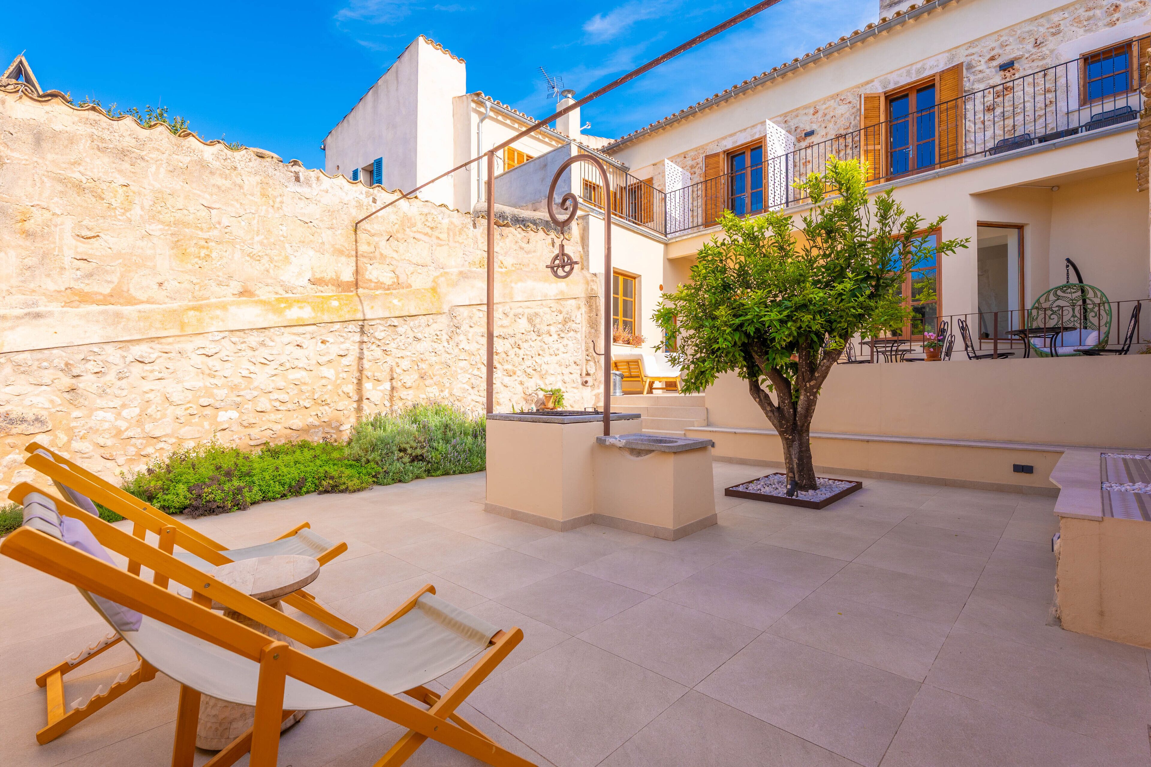 Un patio con mobiliario exterior, un árbol y un muro de piedra.
