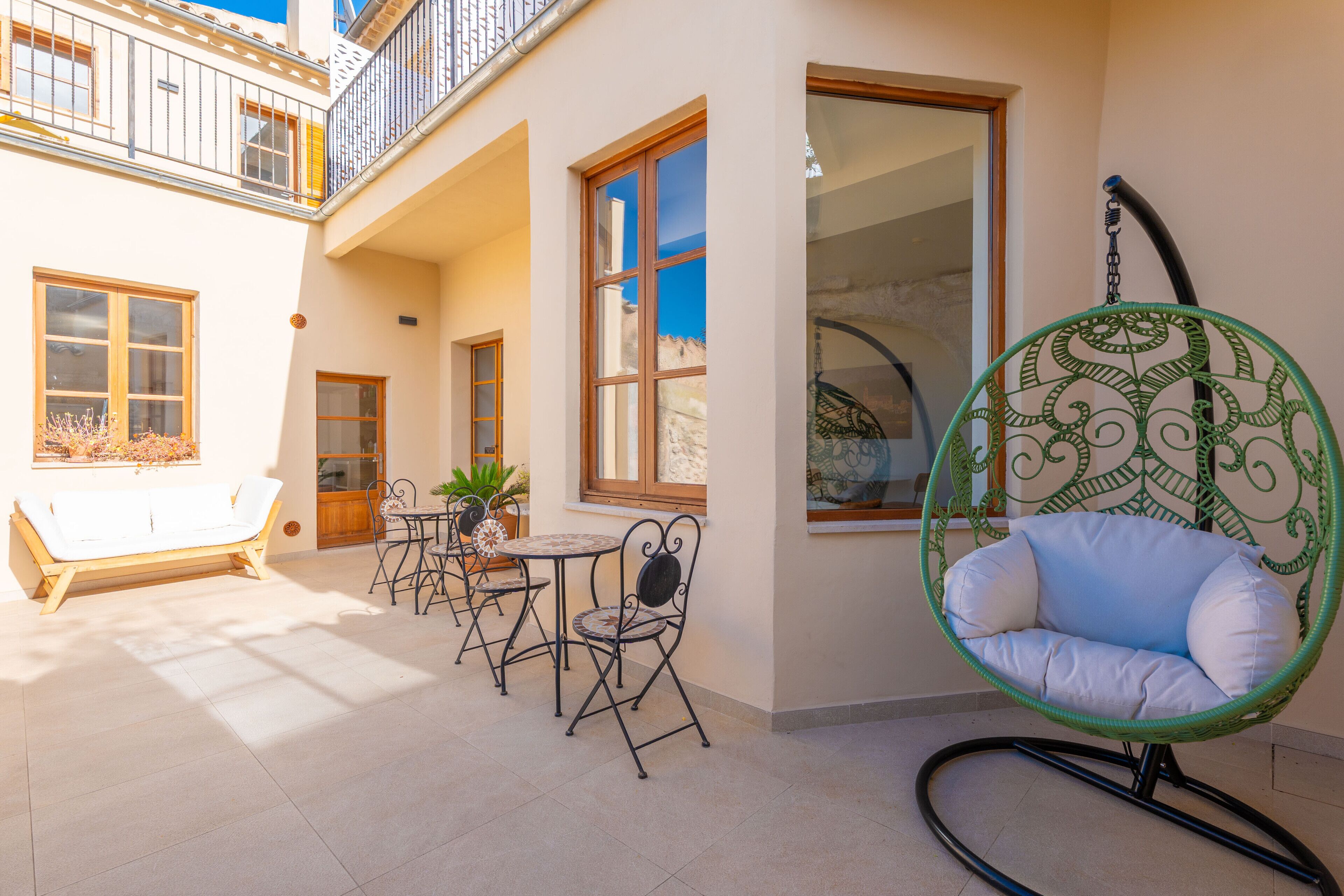 A sunlit patio with a white bathtub, a hanging chair, and a table with chairs.