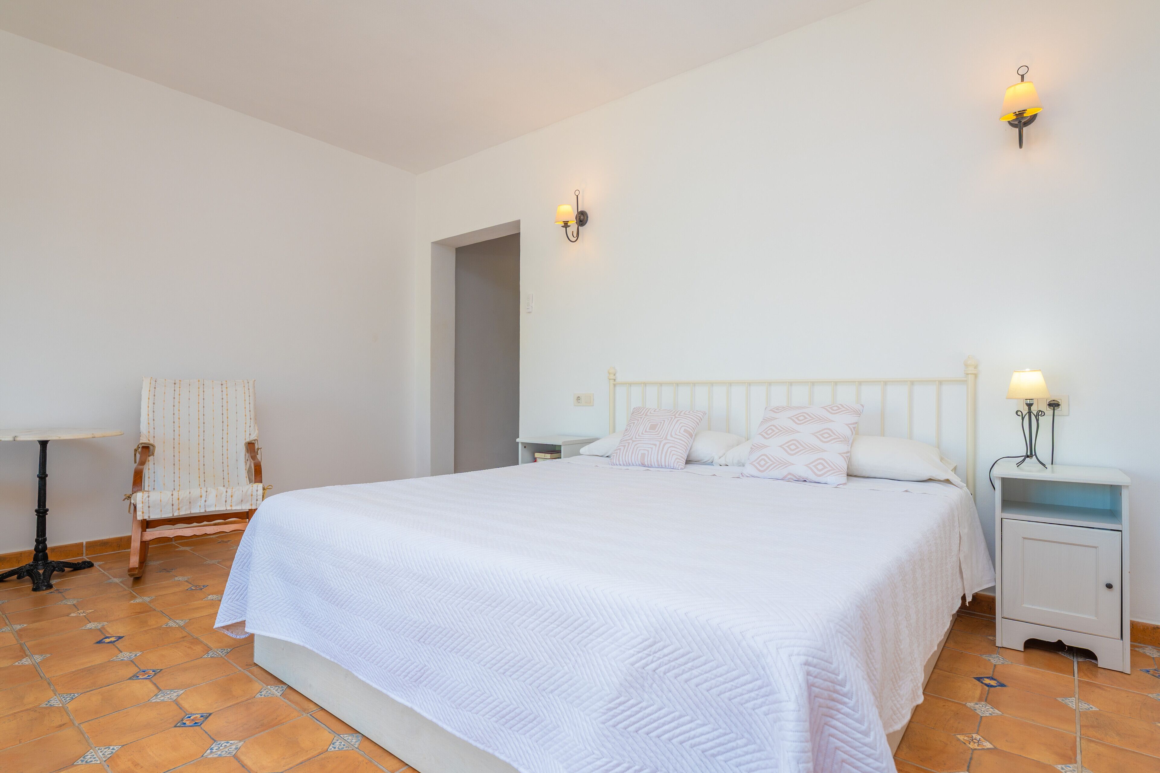 Un dormitorio con una cama grande, dos mesitas de noche, una silla y una pequeña mesa.