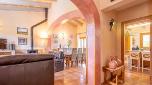 A spacious living area with a brown leather sofa, a dining table with chairs, and a kitchen visible through an archway. - SON GARRETA - Beautiful country house with private pool and free wifi (Campanet)