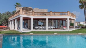 A modern house with a pool, featuring a covered patio with outdoor furniture and a stone facade. - VILLA PORT VERD - Luxury sea-front villa in Cala Bona (Son Servera)