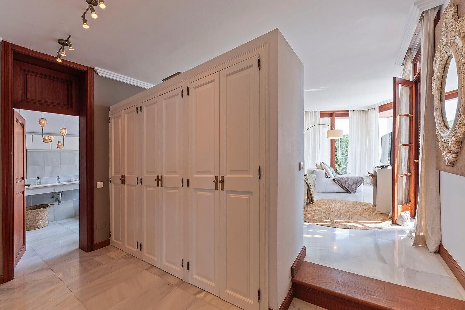 Un couloir avec une grande armoire, une salle de bain avec un lavabo et un miroir, et un espace de vie comprenant un canapé et un tapis.