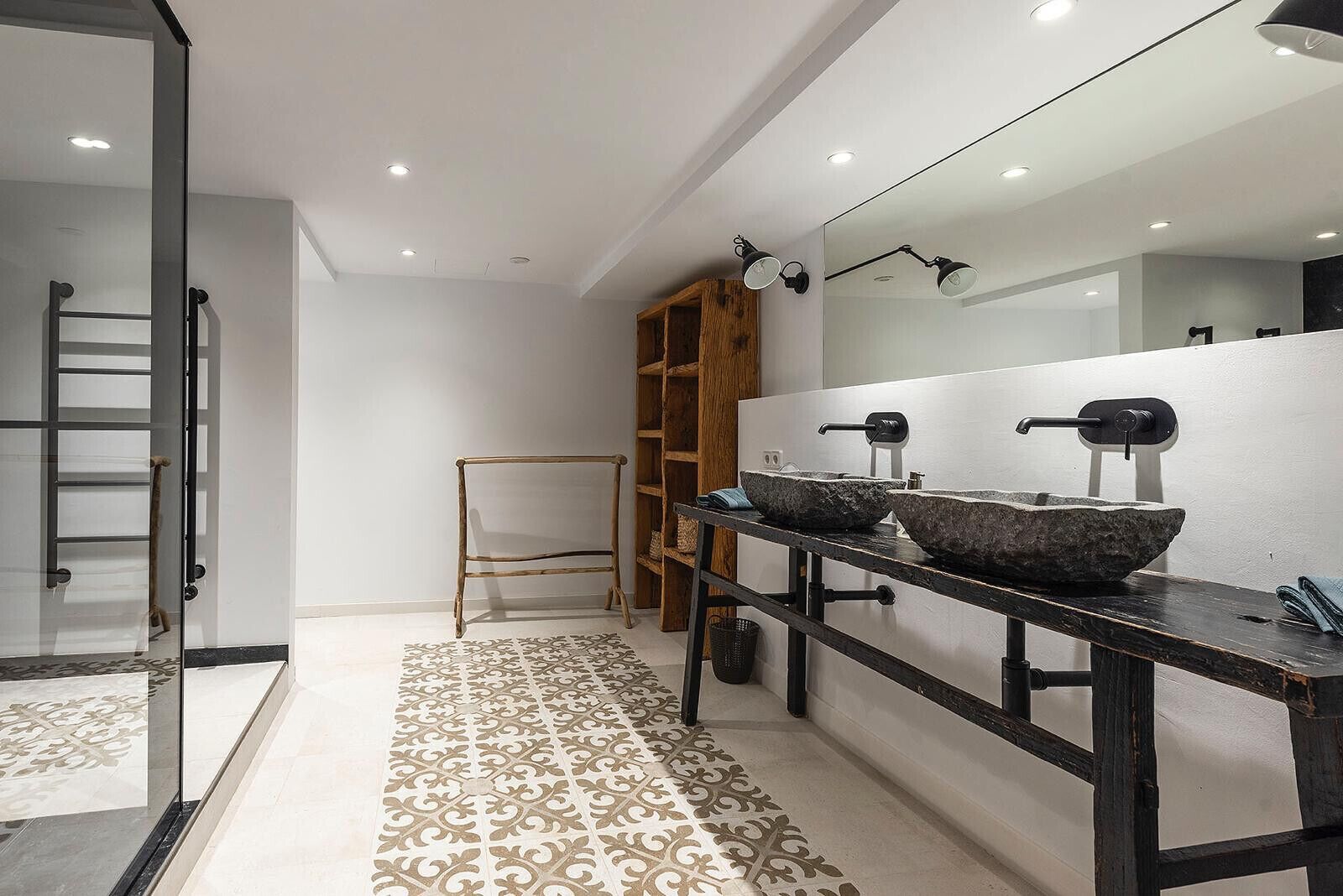 A modern bathroom with a large mirror, two stone sinks, a wooden ladder, and a patterned floor.