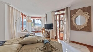 A hotel room with a bed, a TV, a large mirror, and a balcony with a view of the sea. - VILLA PORT VERD - Luxury sea-front villa in Cala Bona (Son Servera)