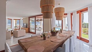 A spacious dining area with a wooden table, woven pendant lights, and a view of the sea. - VILLA PORT VERD - Luxury sea-front villa in Cala Bona (Son Servera)