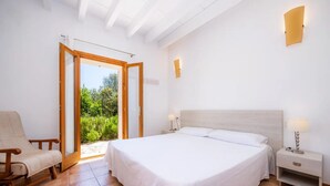 Ein Schlafzimmer mit einem großen Bett, einem Sessel, einem Nachttisch und einer Glastür zum Balkon.
