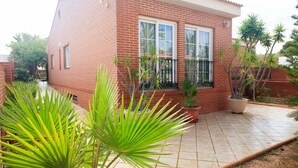 Una casa de ladrillo rojo con un patio empedrado, plantas en macetas y un pequeño jardín.